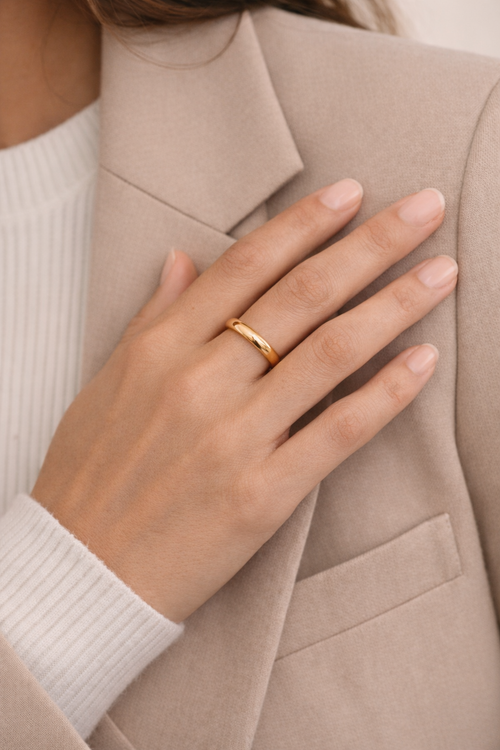Hand wearing a gold ring with a neutral background